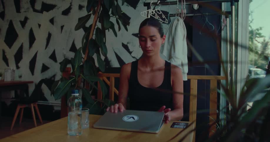 A stylish woman closes her laptop after working in a modern cafe and takes a moment to relax and gaze thoughtfully out the window
