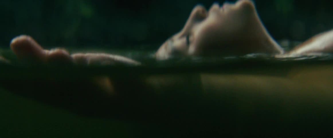 An atmospheric and mysterious close-up of a person's hand and face floating on the surface of murky, dark water