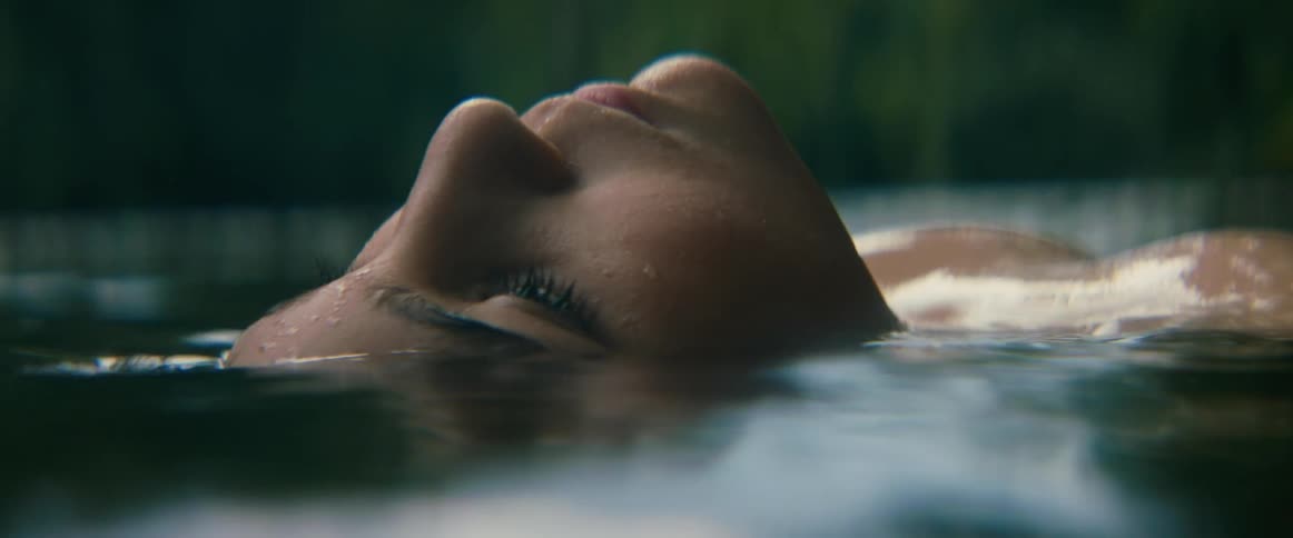 A serene woman's face floats on the surface of calm water as she slowly opens her eyes