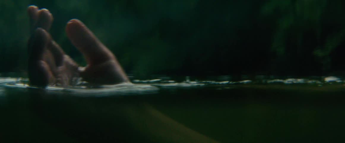 An artistic, moody close-up of a hand gently floating in dark water as a person relaxes on their back