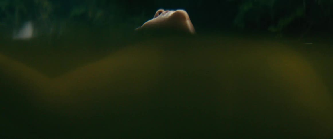 An atmospheric close-up shows a woman peacefully floating on her back in a dark, still body of water
