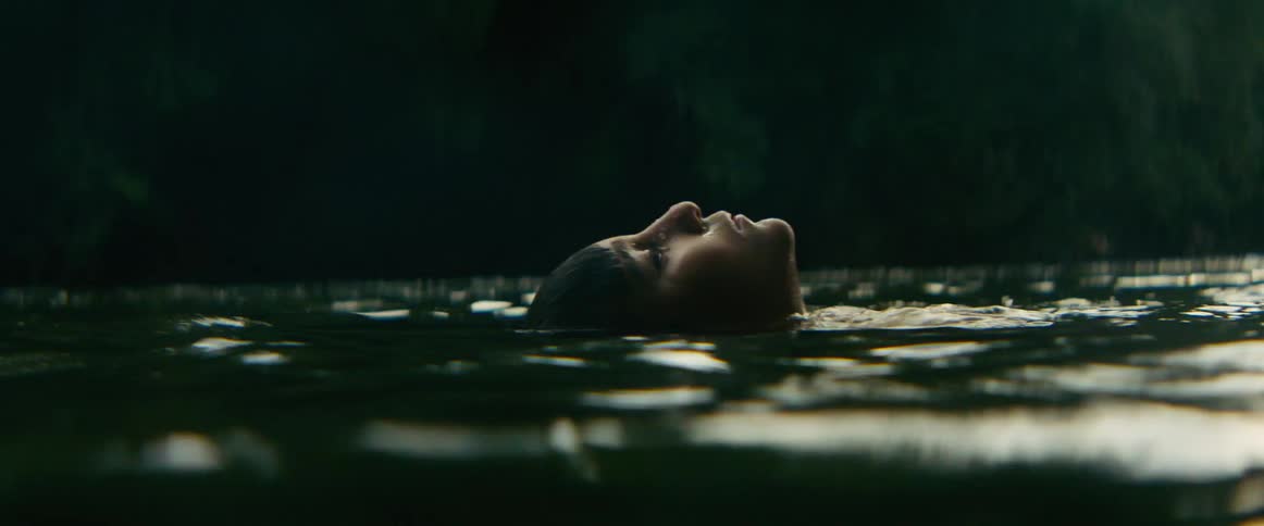 A young boy peacefully floats on his back with eyes closed in a serene river, surrounded by a lush green forest
