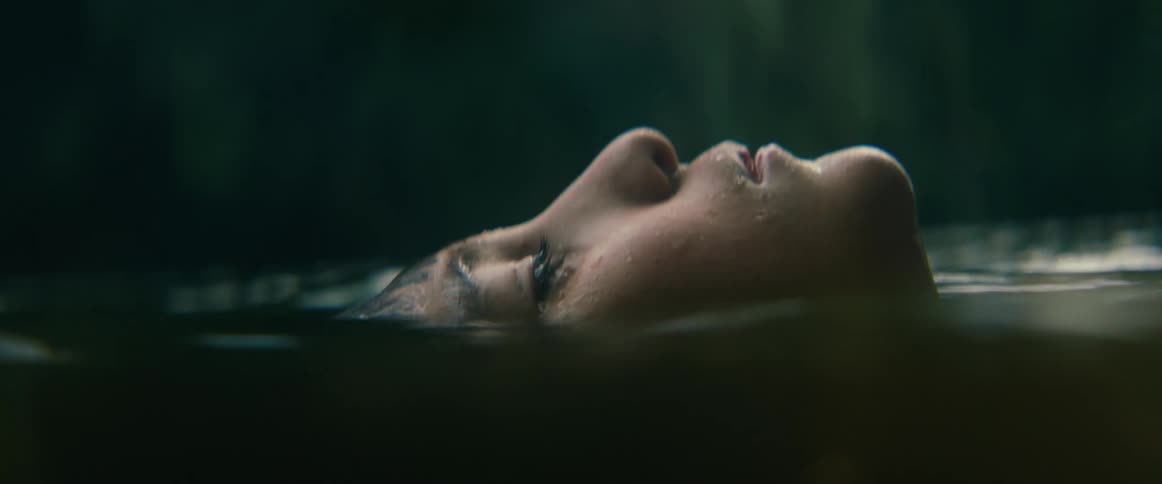 A serene and cinematic close-up of a person's face floating peacefully on the surface of calm, dark water