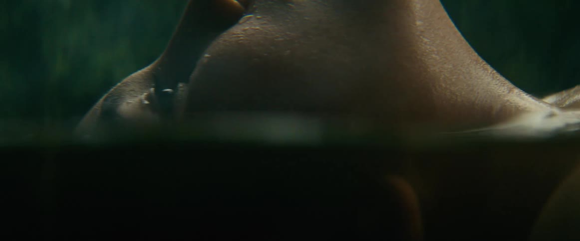 A serene close-up shot shows a person's face floating just above the water's surface as gentle rain begins to fall