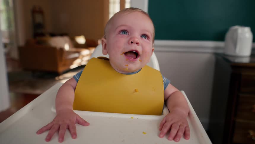 A happy baby with a messy face laughs with joy while sitting in a high chair
