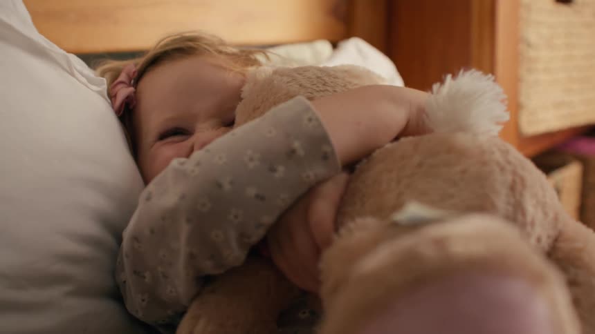 An adorable toddler girl in her pajamas smiles happily as she receives and cuddles her soft stuffed animal in bed