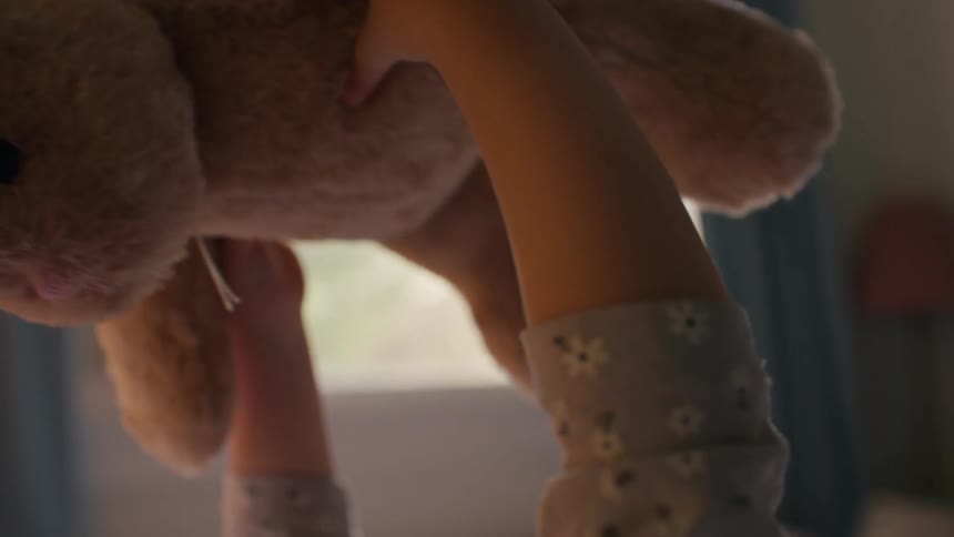 A close-up, slow-motion shot of a child's hands holding up a beloved stuffed bunny rabbit in a sunlit bedroom