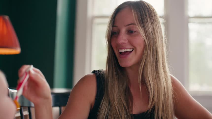 A happy mother smiles and makes funny faces while feeding her baby with a spoon in their dining room