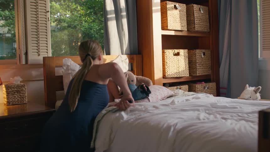 A caring mother walks over to her sick daughter's bed in a sunlit room and takes her temperature
