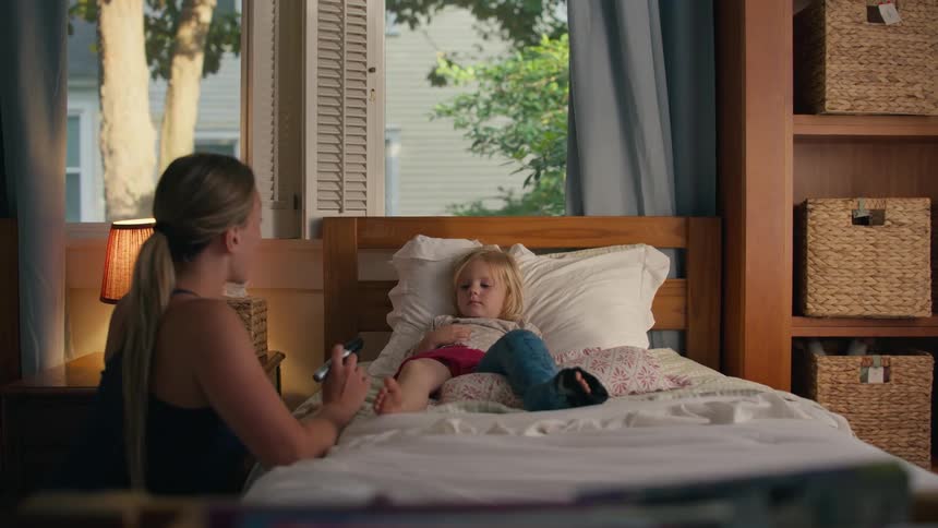 A loving mother comforts her sad daughter with a broken leg in a cast by tickling her toes and making her laugh