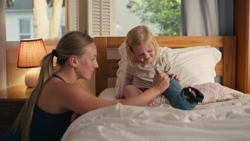 A loving mother smiles as she prepares to sign her happy young daughter's blue leg cast while the child sits in bed