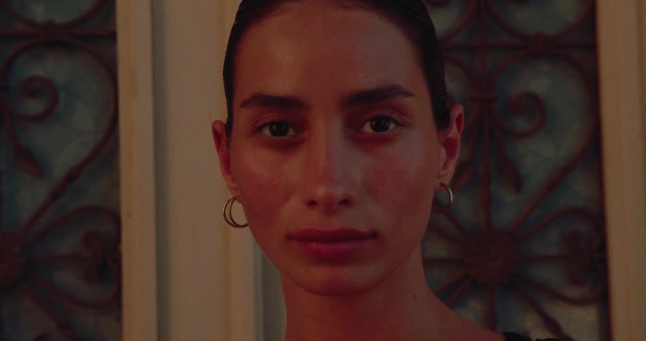 An intimate close-up of a woman's face as she looks directly into the camera, her features illuminated by flickering firelight
