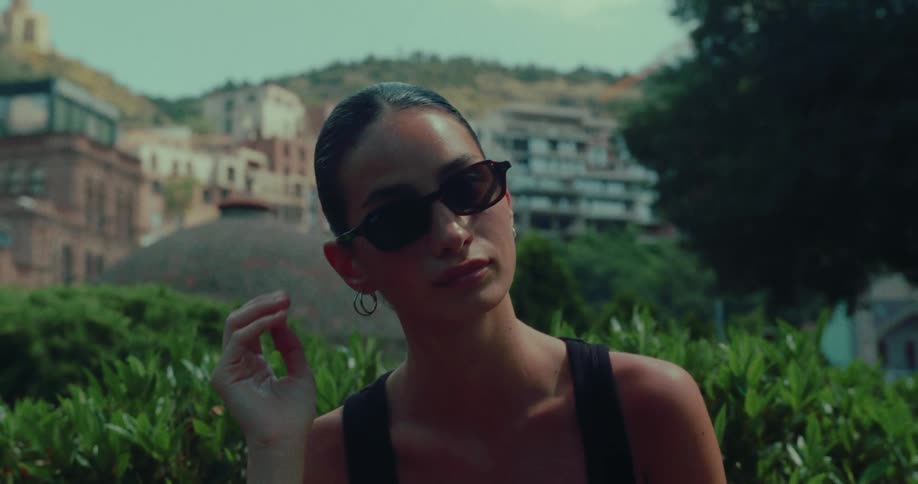 Close-up slow-motion shot of a stylish woman in sunglasses with a scenic European hillside city in the background