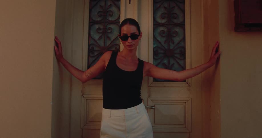 A fashionable young woman with slicked-back hair strikes a pose against an ornate door in the evening light