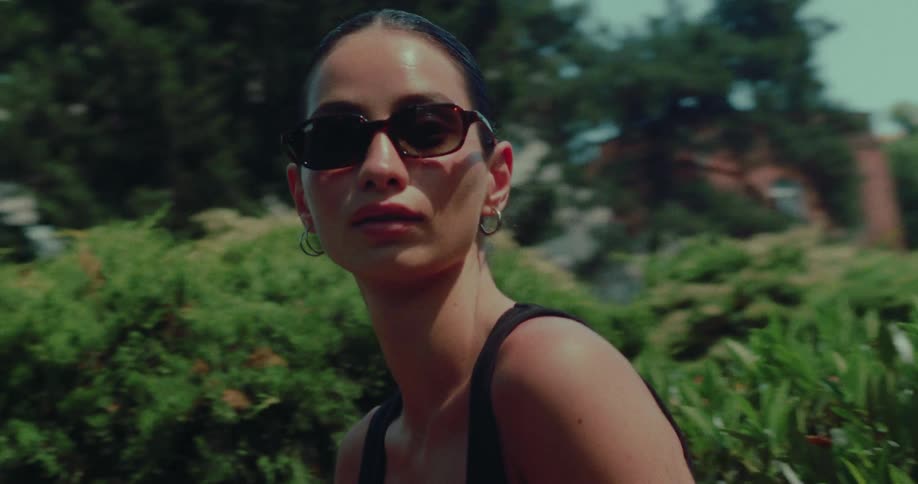 Cinematic slow motion portrait of a stylish woman in sunglasses looking at the camera on a sunny day with a scenic old town in the background