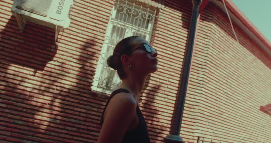 A young woman with her hair in a bun basks in the summer sun on a city street in slow motion