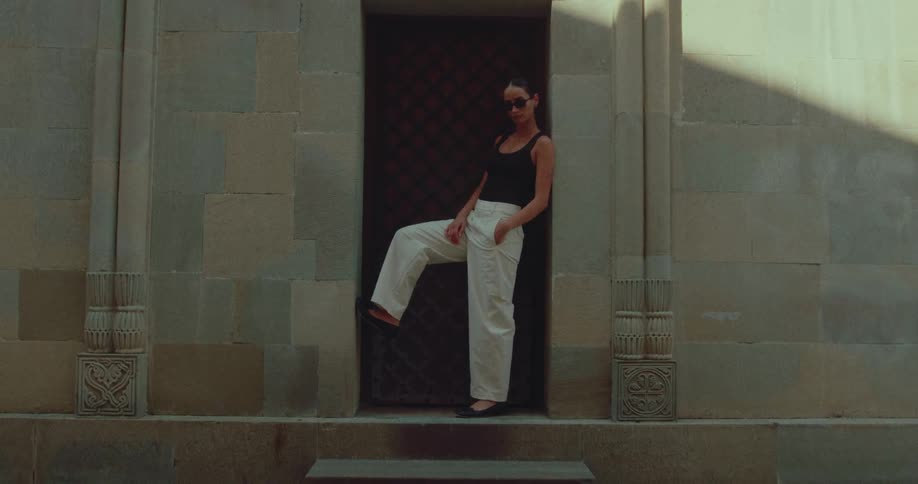 A stylish woman in sunglasses and modern attire strikes a confident pose in an ancient stone doorway