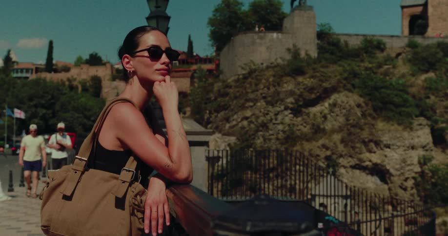 A stylish woman in sunglasses thoughtfully takes in the sights of an old European city on a sunny day