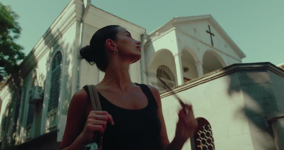 A young woman removes her sunglasses in slow motion while standing in front of a historic white church on a sunny day