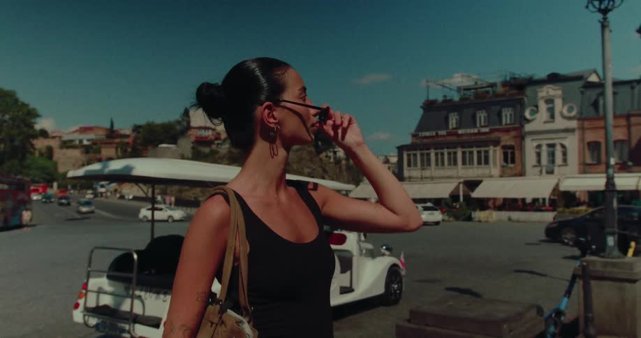 A beautiful brunette woman removes her sunglasses in slow motion while exploring a bustling historic city square on a sunny day