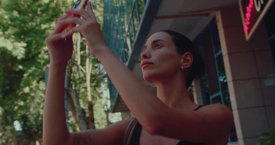 Low angle view of a young woman with tattoos taking a picture with her smartphone on a city street