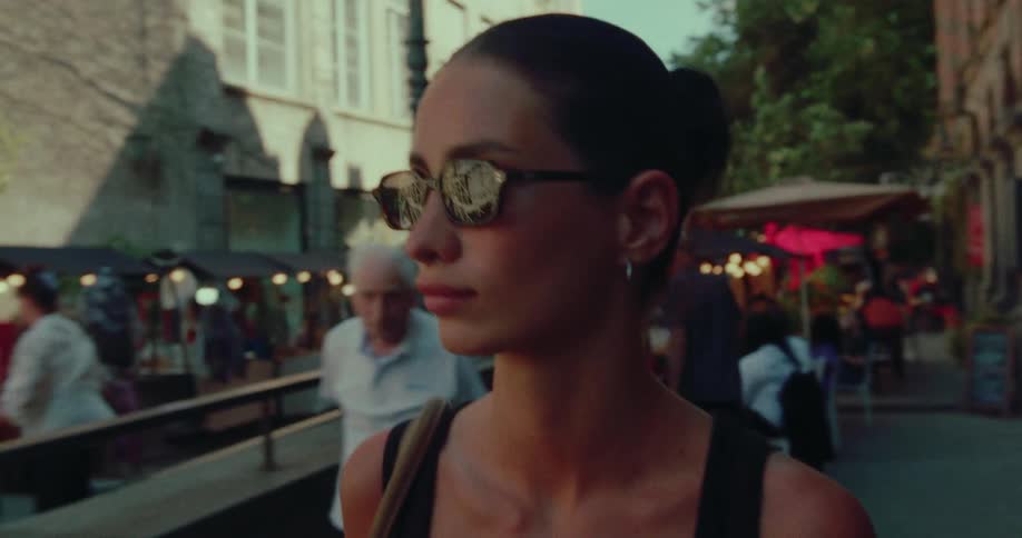 Cinematic slow-motion shot of a beautiful woman with sunglasses strolling through a lively European street market