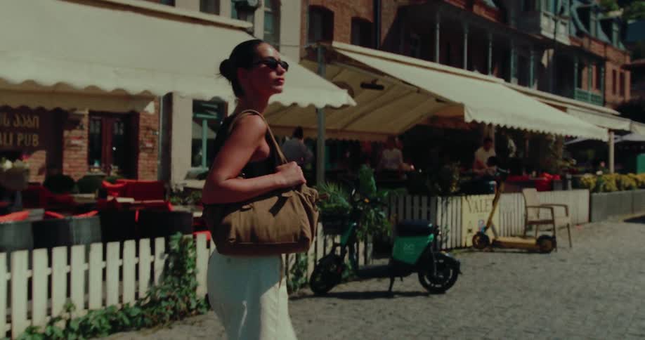 Side-view of a fashionable woman with sunglasses strolling through a charming European city on a sunny day