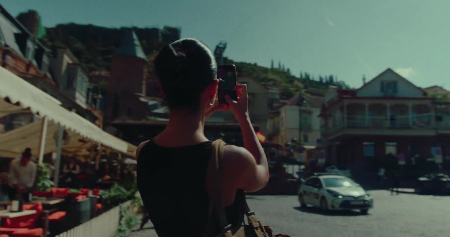 A stylish woman in sunglasses takes a video of a historic European city on her smartphone while exploring on a sunny day