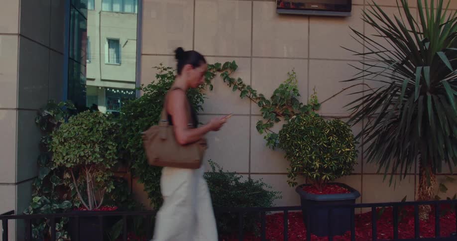 A woman walks down a city street while looking down at her mobile phone in slow motion