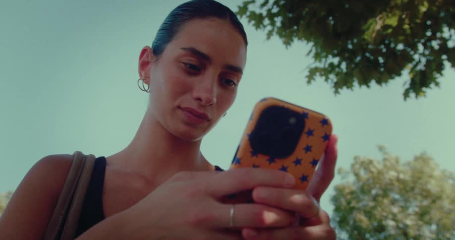 Low angle close-up of a young woman scrolling through her social media feed on a smartphone outdoors