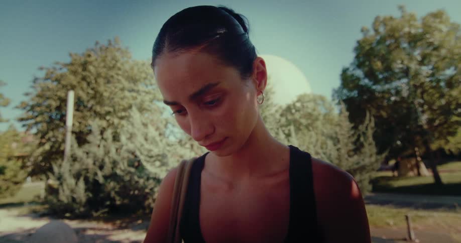 Close-up of a pensive young woman scrolling on her smartphone in a sunlit park
