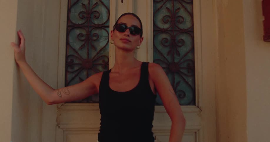 A stylish woman wearing sunglasses poses confidently against an ornate vintage door as the camera slowly pulls out