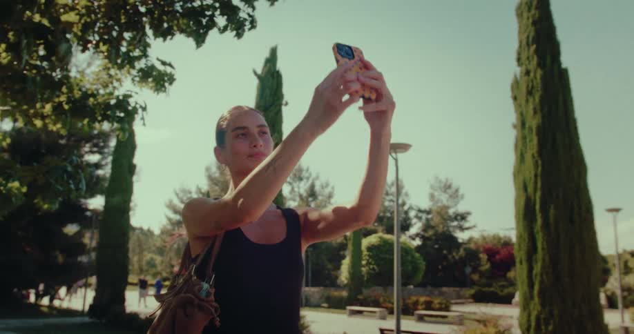Happy young woman with short hair takes a selfie on her phone while enjoying a sunny day in a beautiful park
