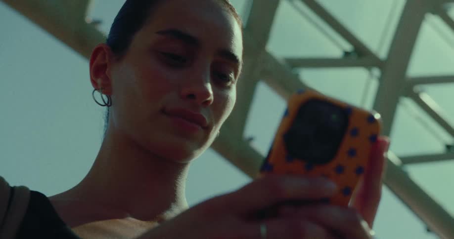 A stylish young woman scrolls through her smartphone from a low-angle perspective under a modern glass roof