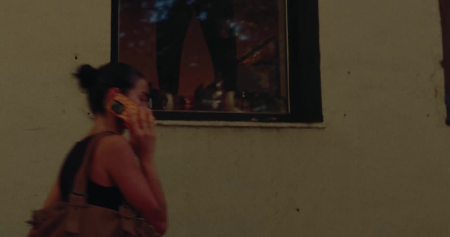 A young woman walks down a city street at night while having a conversation on her phone