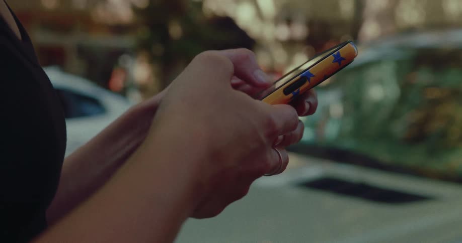 A close-up of a woman's hands scrolling and texting on a smartphone on a city street