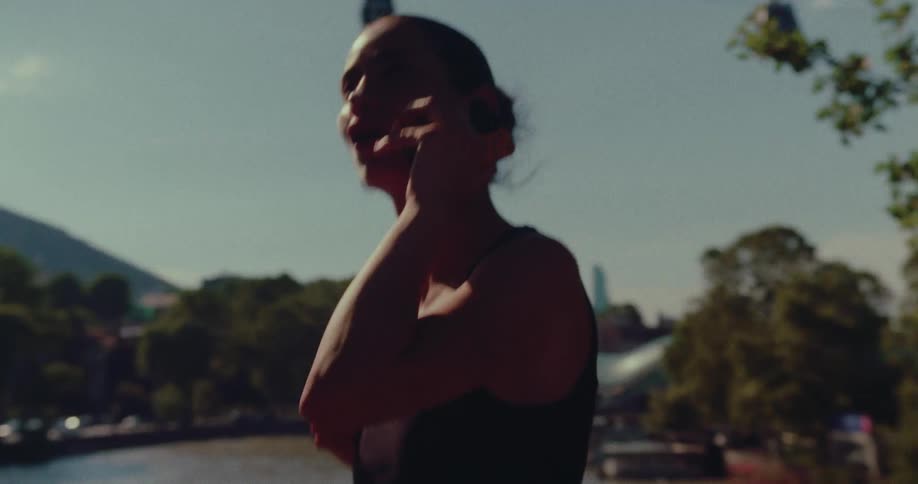 A silhouetted woman has an animated phone conversation on a sunny bridge overlooking a river with cable cars in the background