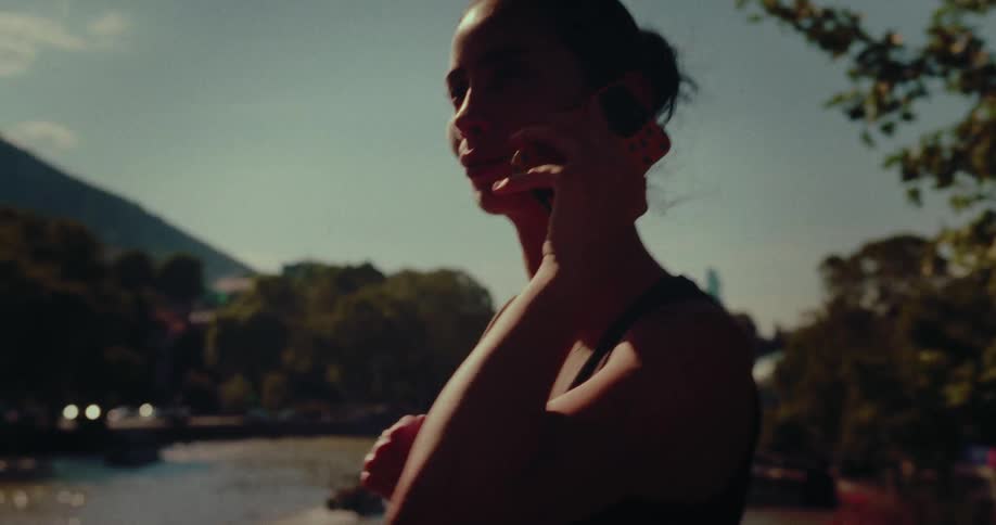 Close-up profile shot of a woman on a phone call, silhouetted by the bright sun in a park