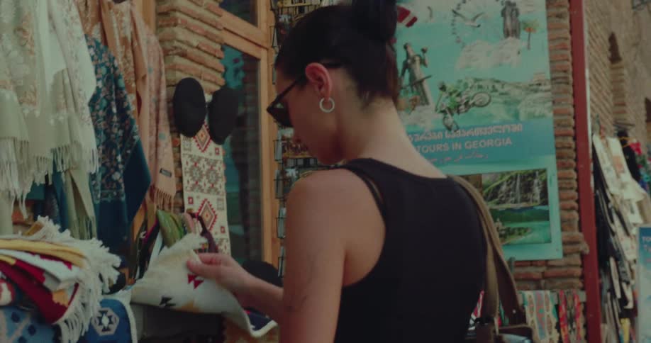 A stylish woman in sunglasses shops for traditional woven rugs and textiles at an outdoor market