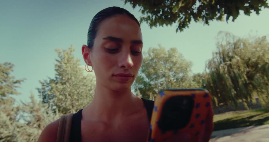 Low angle close-up of a serious young woman scrolling on her smartphone while standing in a park