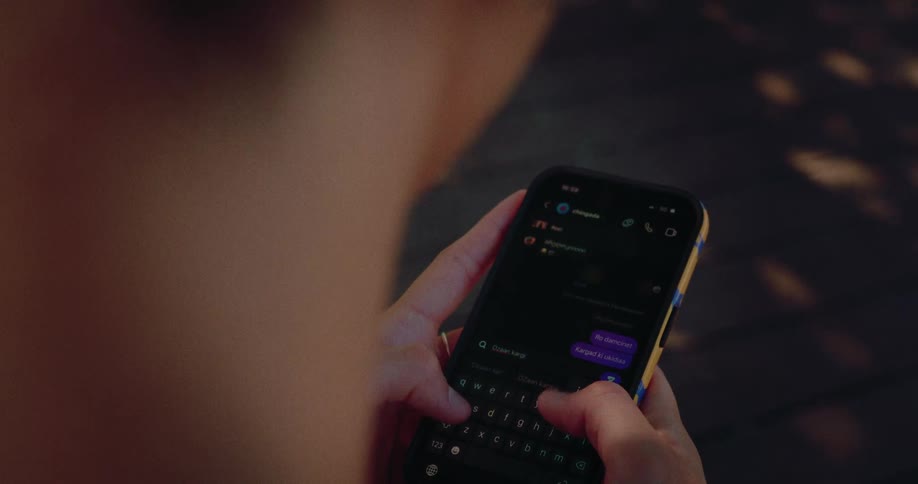 An over-the-shoulder close-up of a person's hands typing a message on a smartphone's touch screen keyboard