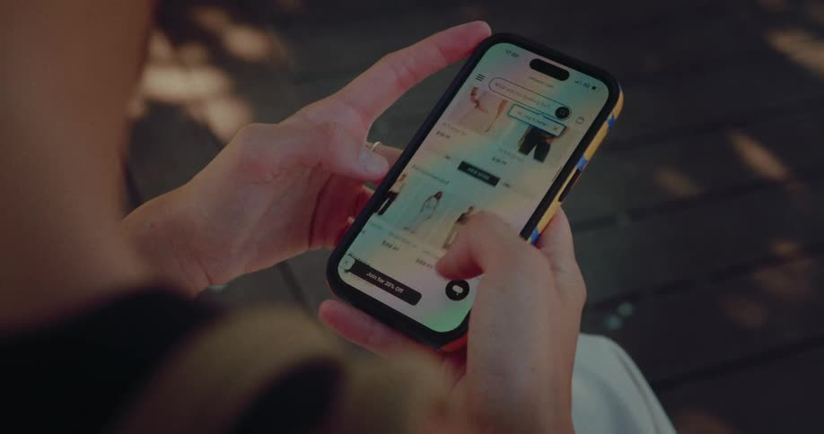 An over-the-shoulder view of a person online shopping for clothes on their smartphone