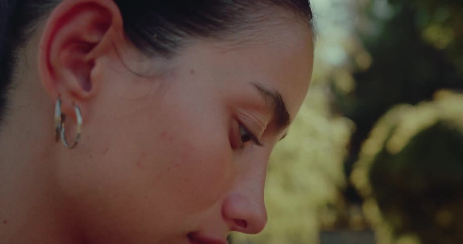 A close-up of a young woman's hands scrolling on her phone, then panning up to her focused face in a sunlit park