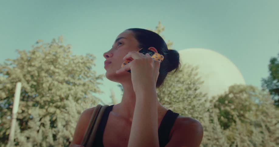 A stylish young woman pulls her phone from her bag and answers a call while enjoying a sunny day in the park