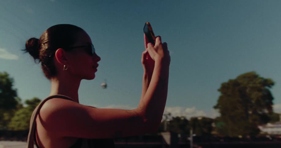 A stylish woman in sunglasses films a scenic view of a historic church on a cliff in an old European city on a sunny day