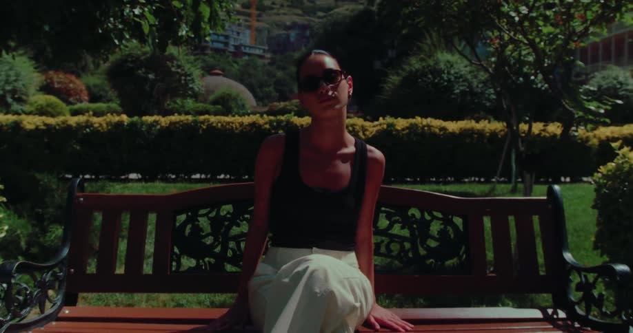 A stylish woman wearing sunglasses relaxes on a park bench on a sunny summer day