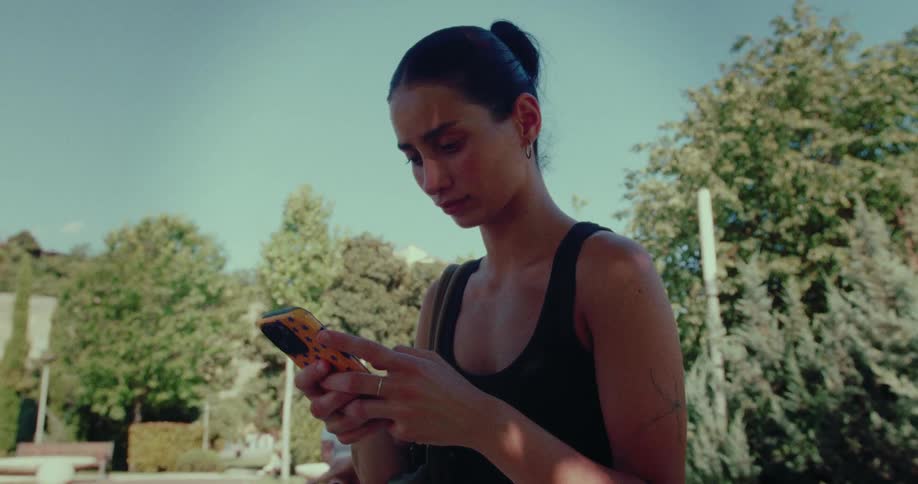 Low-angle shot of a focused young woman scrolling through her phone on a sunny day in the park