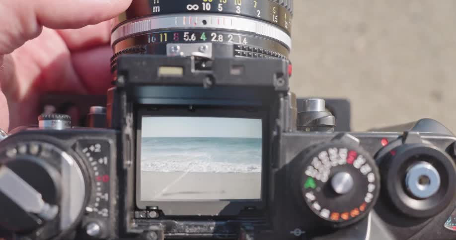 Looking through the waist-level viewfinder of a vintage film camera to focus on ocean waves at the beach