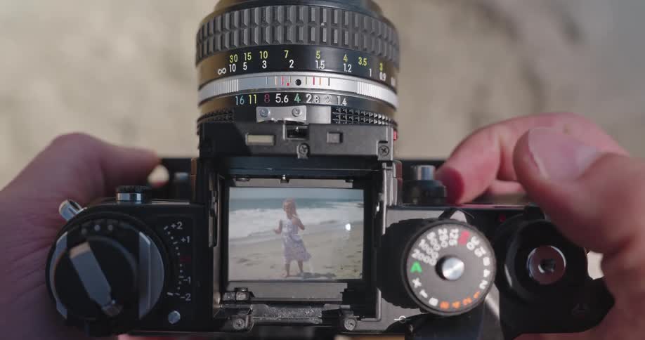 A photographer's point of view as they focus a vintage film camera to take a picture of a little girl on the beach