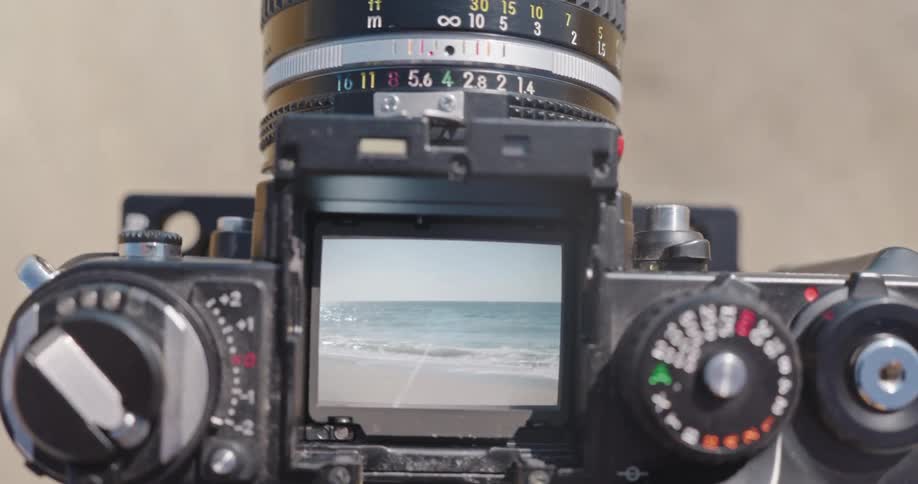 POV shot through a vintage camera's open viewfinder captures the serene ocean waves lapping at the shore